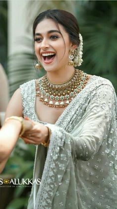 a woman in a white sari smiles and holds her hand out