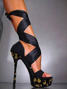 a woman's legs wearing high heeled shoes with black and gold print straps