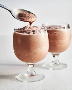 two glasses filled with chocolate pudding on top of a white table next to a spoon