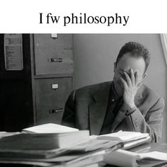 a man sitting at a desk in front of a pile of books with his hands on his face