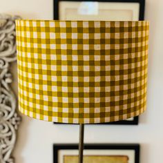 a yellow and white checkered lampshade next to a wall with pictures on it