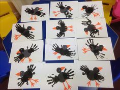 six handprints of black and orange birds on white paper with blue chairs in the background