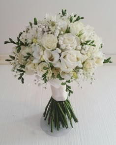 a bouquet of white roses and greenery in a vase on top of a table