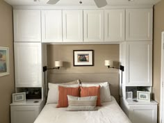 a bed with white headboard and pillows under a ceiling fan in a room that has beige walls