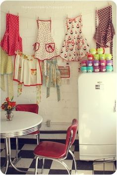 there are many aprons hanging on the wall next to a table with chairs and a refrigerator