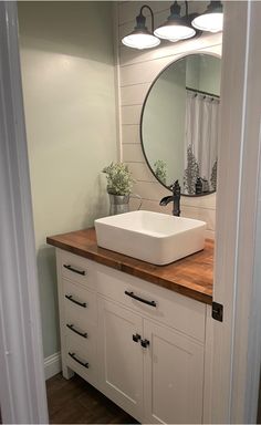 a white sink sitting under a bathroom mirror next to a wooden counter topped with a potted plant