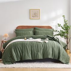 a bed with green bedspread and pillows in a white room next to a potted plant