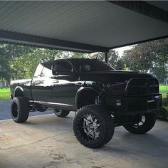 a large black truck parked under a covered parking lot with trees in the back ground