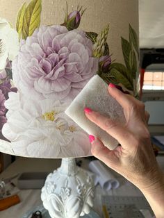 a woman is holding up a lamp shade with flowers on it and she has her hand over the fabric