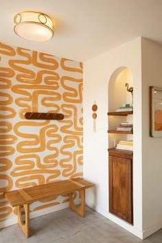 a wooden bench sitting in front of a wall with an orange design on it's side