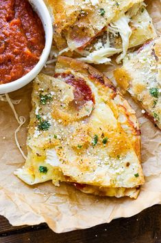 pizza slices with sauce and parmesan cheese on top sitting on wax paper next to a bowl