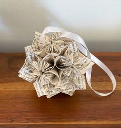 an origami flower made out of book pages on a wooden table with white ribbon