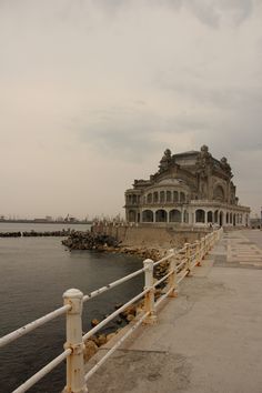 an old building sitting on the side of a body of water next to a pier