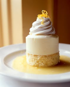 a small dessert on a white plate with yellow icing and lemon zest garnish