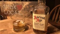 a bottle of ancient age bourbon whiskey next to a glass with ice on the table