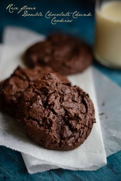 two chocolate cookies sitting on top of paper next to a glass of milk