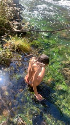 a young boy is standing in the water and looking down at the ground below him