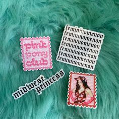 three stickers that are sitting on top of a green fur covered surface with words