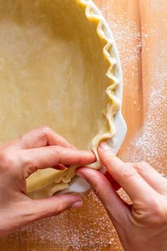 two hands are placing dough into a pie crust