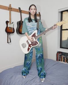 a woman standing on top of a bed holding an electric guitar