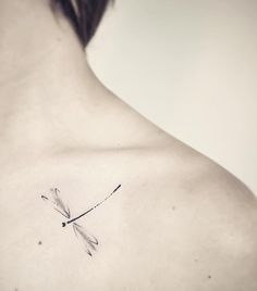 the back of a woman's shoulder with a small dragonfly tattoo on it