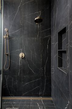 a walk in shower sitting next to a black tiled wall and floor covered in grey marble