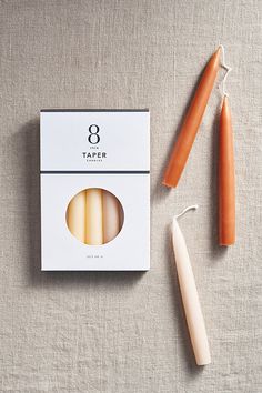 an orange candle next to a white box and two candles on a gray tablecloth