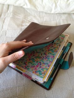 a person holding an open wallet on top of a bed with books and binders