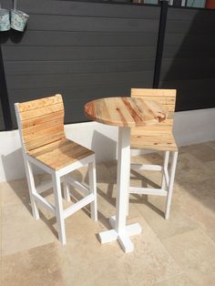 two wooden chairs sitting next to each other near a table and chair on the ground