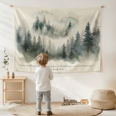 a little boy standing in front of a wall hanging with a forest scene on it