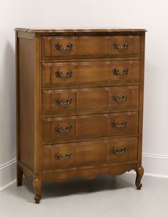 an old wooden dresser with many drawers and knobs on the bottom drawer, against a white wall