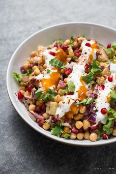 a white bowl filled with lots of food on top of a gray countertop next to a spoon