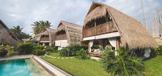 a house with thatched roof next to a swimming pool and lush green lawn area