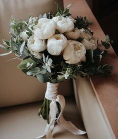 a bridal bouquet with white flowers and greenery on the side of a couch