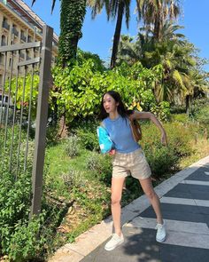 a young woman is playing frisbee on the sidewalk near some trees and bushes