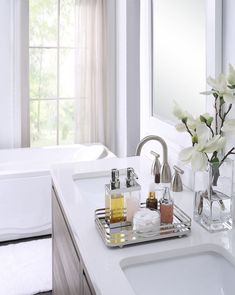 a bathroom sink sitting under a mirror next to a bathtub with flowers in it