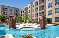 an outdoor swimming pool with lounge chairs and water features surrounded by apartment buildings in the background