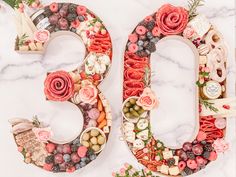 the number 50 is made up of flowers and fruits on a marble surface with greenery