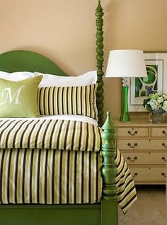 a green bed with striped sheets and pillows on top of it next to a dresser