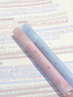 two pink and blue pencils sitting on top of a piece of paper with writing