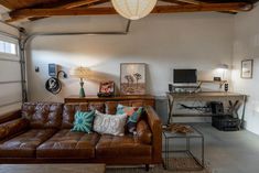 a brown leather couch sitting in a living room next to a wooden table and lamp