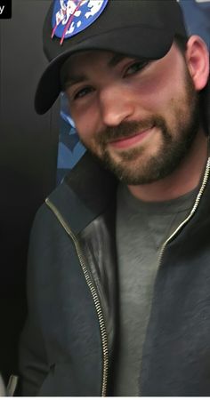 a man with a beard wearing a baseball cap and smiling at the camera while he is taking a selfie