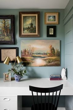 a white desk topped with a black chair next to a painting on the wall above it