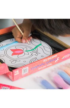 a child is drawing on a coloring book with crayons and pencils in front of it