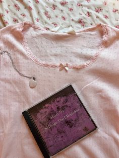 a book is laying on the bed next to a pink shirt with flowers and beads