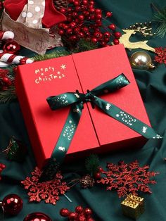 a red gift box with green ribbon sitting on top of a table covered in christmas decorations