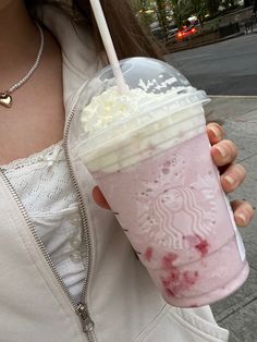 a woman holding up a pink drink with whipped cream on it and a straw in her hand