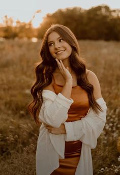 a beautiful young woman standing in a field with her hands on her face and smiling at the camera