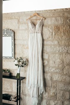 a wedding dress hanging on a brick wall next to a mirror and vase with flowers