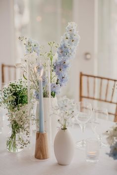 the table is set with white and blue flowers in vases, candles, and wine glasses